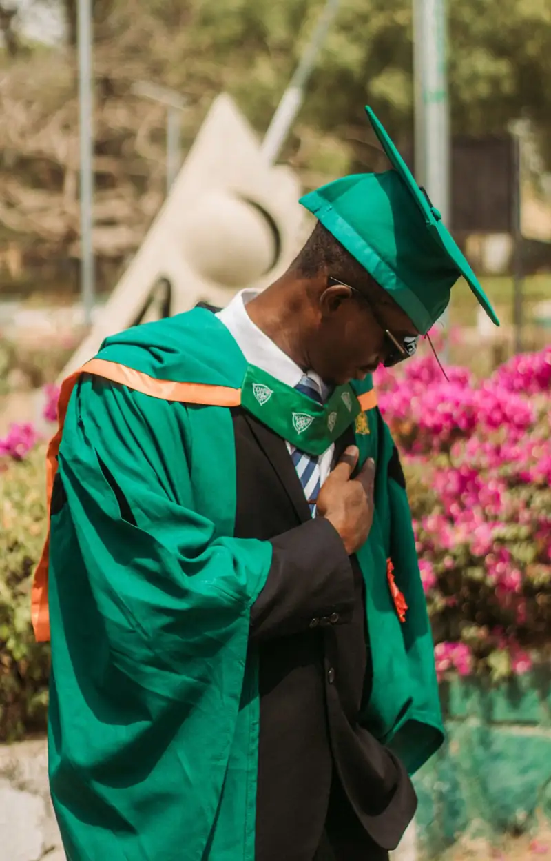 Close view of a graduate in a black gown and red stole in warm outdoor light. Stock photo from Pexels, not a Nafasi student.